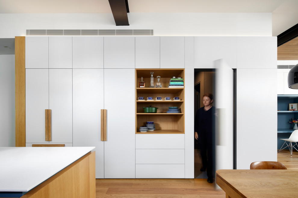 Design ideas for a mid-sized contemporary u-shaped open plan kitchen in Melbourne with an undermount sink, flat-panel cabinets, blue cabinets, solid surface benchtops, grey splashback, ceramic splashback, black appliances, medium hardwood floors, with island, beige floor and white benchtop.