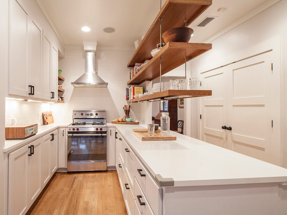 This is an example of a transitional u-shaped separate kitchen in Austin with shaker cabinets, white cabinets, white splashback, subway tile splashback and stainless steel appliances.