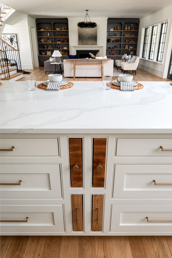 Traditional kitchen in Charlotte with a belfast sink, beaded cabinets, white cabinets, engineered stone countertops, white splashback, engineered quartz splashback, coloured appliances, light hardwood flooring, an island, brown floors and white worktops.
