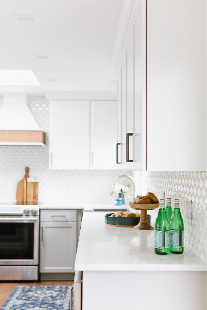 Mid-sized transitional u-shaped medium tone wood floor and brown floor open concept kitchen photo with an undermount sink, shaker cabinets, white cabinets, quartz countertops, white backsplash, porcelain backsplash, stainless steel appliances, an island and white countertops
