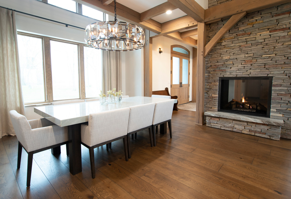 Example of a mountain style medium tone wood floor and exposed beam dining room design with white walls, a two-sided fireplace and a stacked stone fireplace