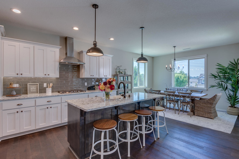 Mid-sized country eat-in kitchen in Portland with a farmhouse sink, flat-panel cabinets, white cabinets, quartzite benchtops, grey splashback, subway tile splashback, stainless steel appliances, medium hardwood floors, with island and white benchtop.
