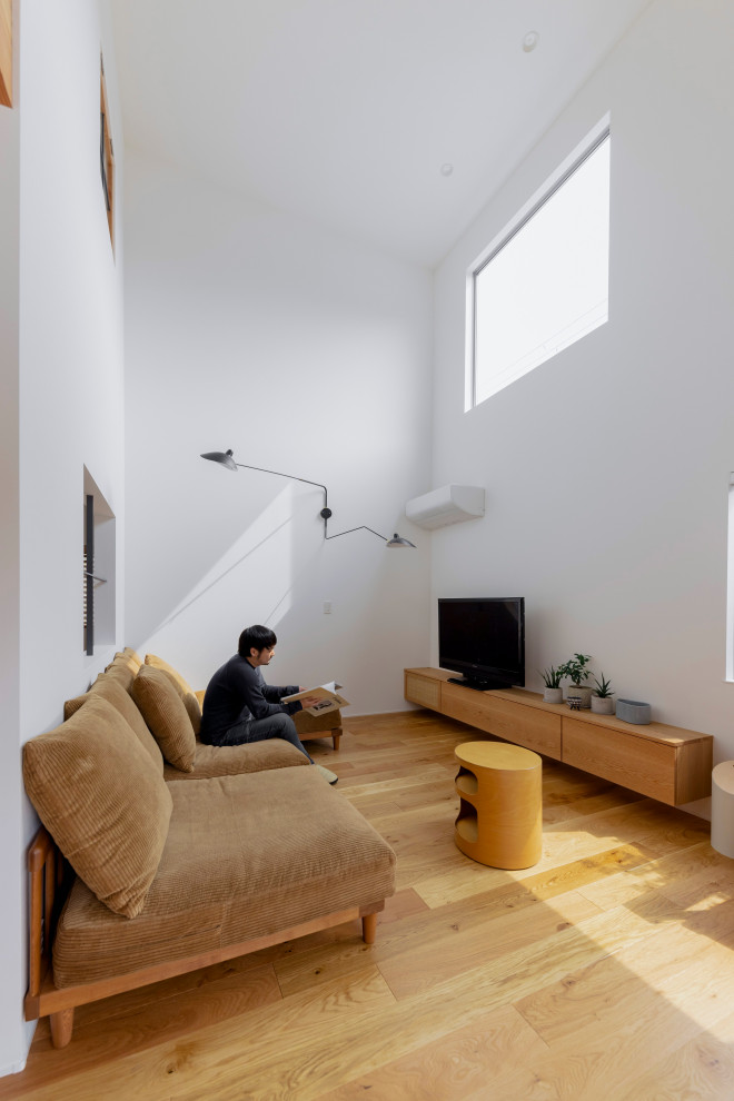 Foto på ett litet nordiskt separat vardagsrum, med ett bibliotek, vita väggar, mellanmörkt trägolv, en fristående TV och beiget golv