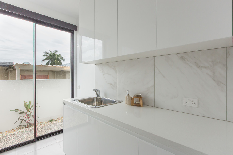 Inspiration for a mid-sized contemporary single-wall dedicated laundry room in Gold Coast - Tweed with a drop-in sink, flat-panel cabinets, white cabinets, quartz benchtops, white walls, ceramic floors and a side-by-side washer and dryer.