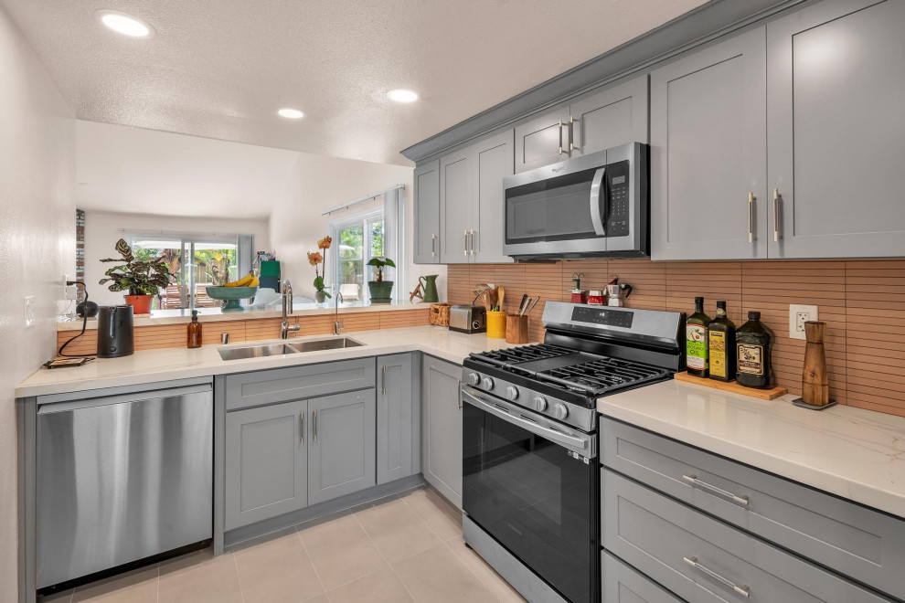 Mid-sized transitional l-shaped ceramic tile and beige floor eat-in kitchen photo with shaker cabinets, an undermount sink, gray cabinets, stainless steel appliances, white countertops, quartzite countertops, orange backsplash, ceramic backsplash and no island