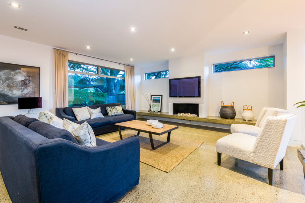 This is an example of a large contemporary open concept living room in Auckland with white walls, concrete floors, a standard fireplace and a wall-mounted tv.