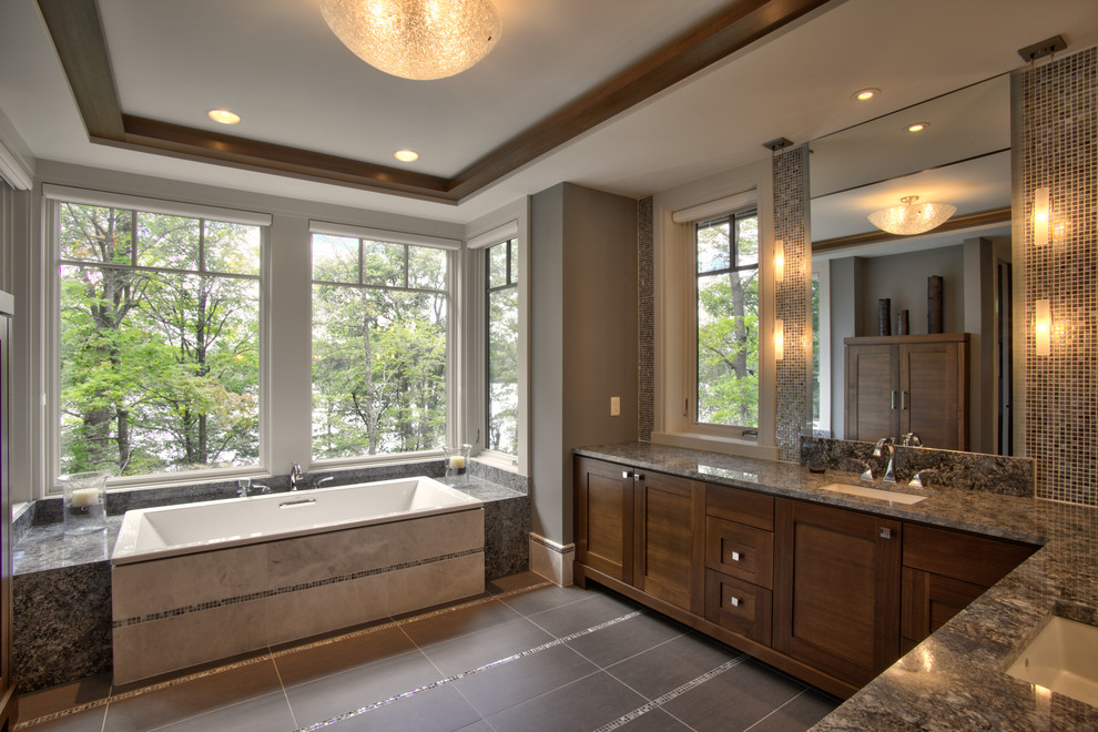 Photo of a mid-sized modern master bathroom in Minneapolis with shaker cabinets, brown cabinets, a drop-in tub, gray tile, mosaic tile, grey walls, ceramic floors, an undermount sink, granite benchtops, grey floor, grey benchtops, a double vanity, a built-in vanity and vaulted.