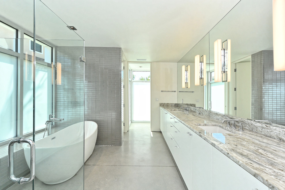 Inspiration for a mid-sized modern master bathroom in Tampa with flat-panel cabinets, white cabinets, a freestanding tub, a corner shower, gray tile, ceramic tile, white walls, concrete floors, an undermount sink, granite benchtops, grey floor, a hinged shower door and grey benchtops.