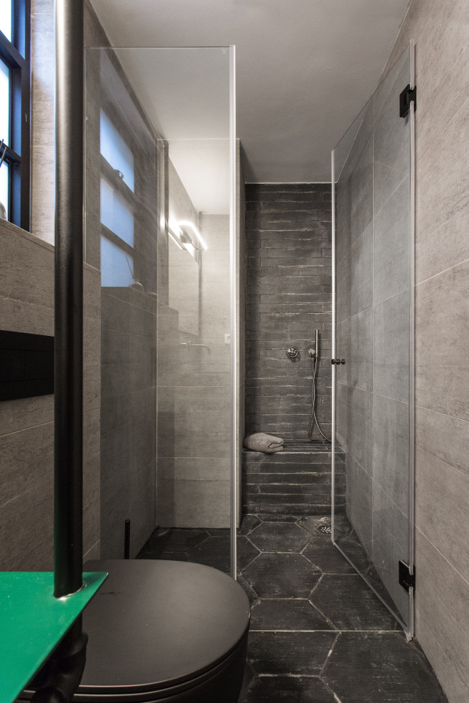 Small industrial 3/4 bathroom in Tel Aviv with open cabinets, green cabinets, a curbless shower, a wall-mount toilet, gray tile, porcelain tile, grey walls, porcelain floors, a console sink, stainless steel benchtops, black floor, a hinged shower door and green benchtops.