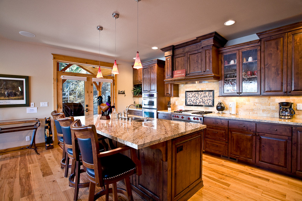 Mountain style kitchen photo in Seattle with raised-panel cabinets, dark wood cabinets, beige backsplash, stone tile backsplash and stainless steel appliances