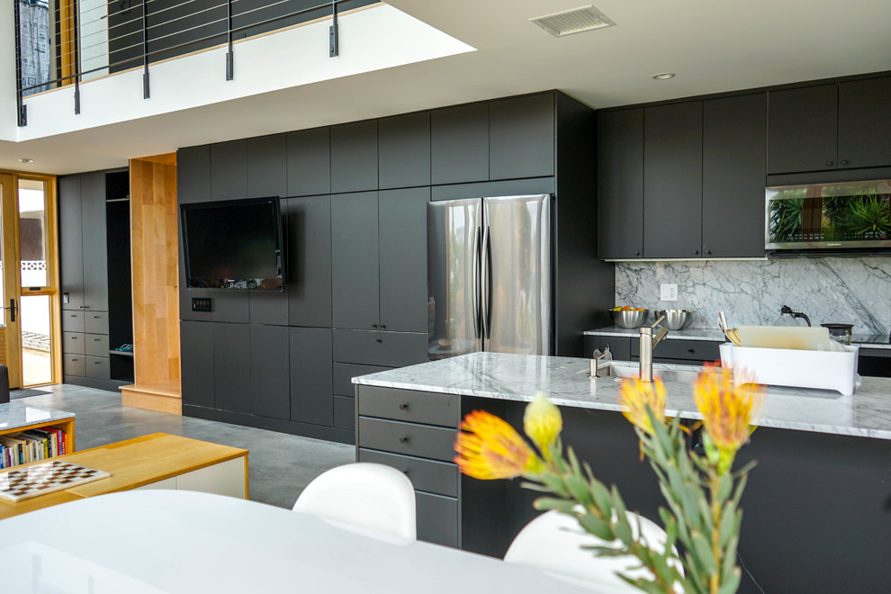 Photo of a mid-sized modern single-wall open plan kitchen in Los Angeles with grey floor, a double-bowl sink, flat-panel cabinets, black cabinets, quartzite benchtops, grey splashback, marble splashback, stainless steel appliances, concrete floors, with island, grey benchtop and vaulted.