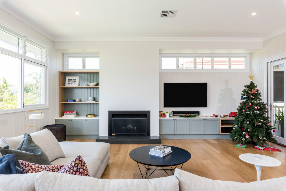 Transitional formal enclosed living room in Brisbane with white walls, medium hardwood floors, a standard fireplace, a wall-mounted tv and beige floor.