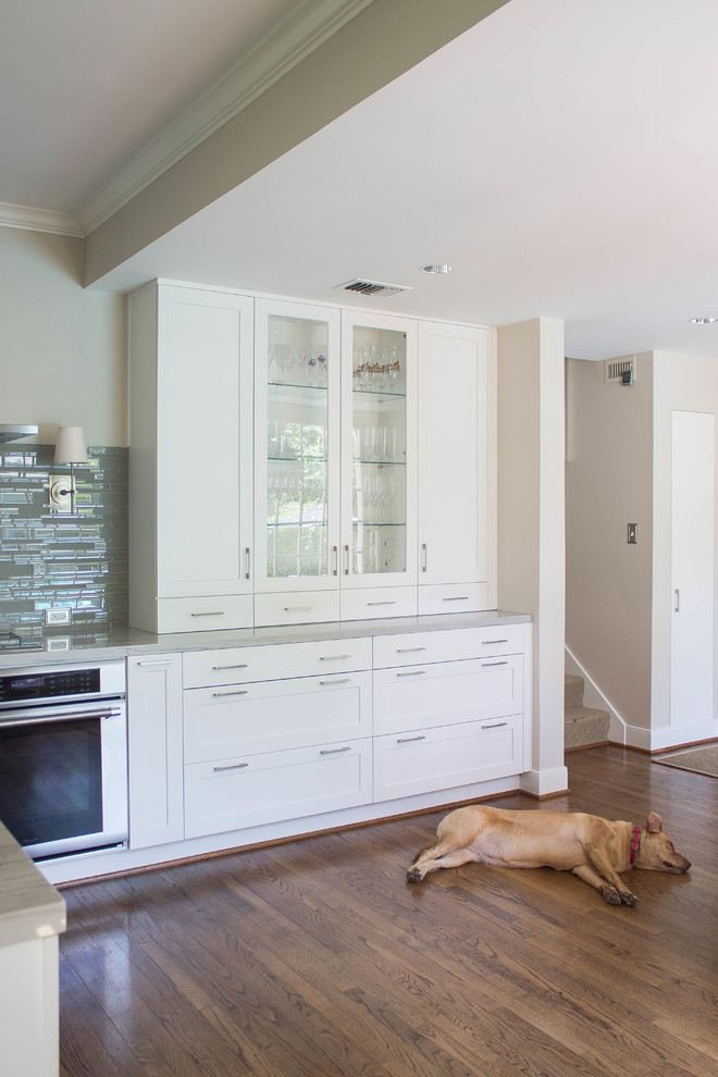 Inspiration for a large transitional l-shaped dark wood floor open concept kitchen remodel in Houston with a double-bowl sink, shaker cabinets, white cabinets, quartzite countertops, gray backsplash, glass tile backsplash, stainless steel appliances and an island