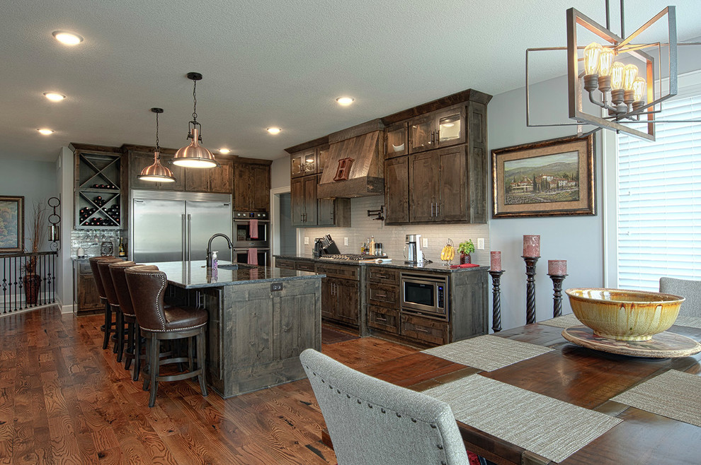 Inspiration for a country eat-in kitchen in Kansas City with an undermount sink, shaker cabinets, brown cabinets, granite benchtops, grey splashback, subway tile splashback, stainless steel appliances, medium hardwood floors, with island, brown floor and brown benchtop.