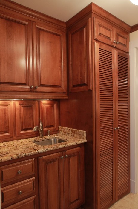 This is an example of a large traditional galley dedicated laundry room in Wilmington with an undermount sink, raised-panel cabinets, dark wood cabinets, granite benchtops, white walls, porcelain floors and a concealed washer and dryer.