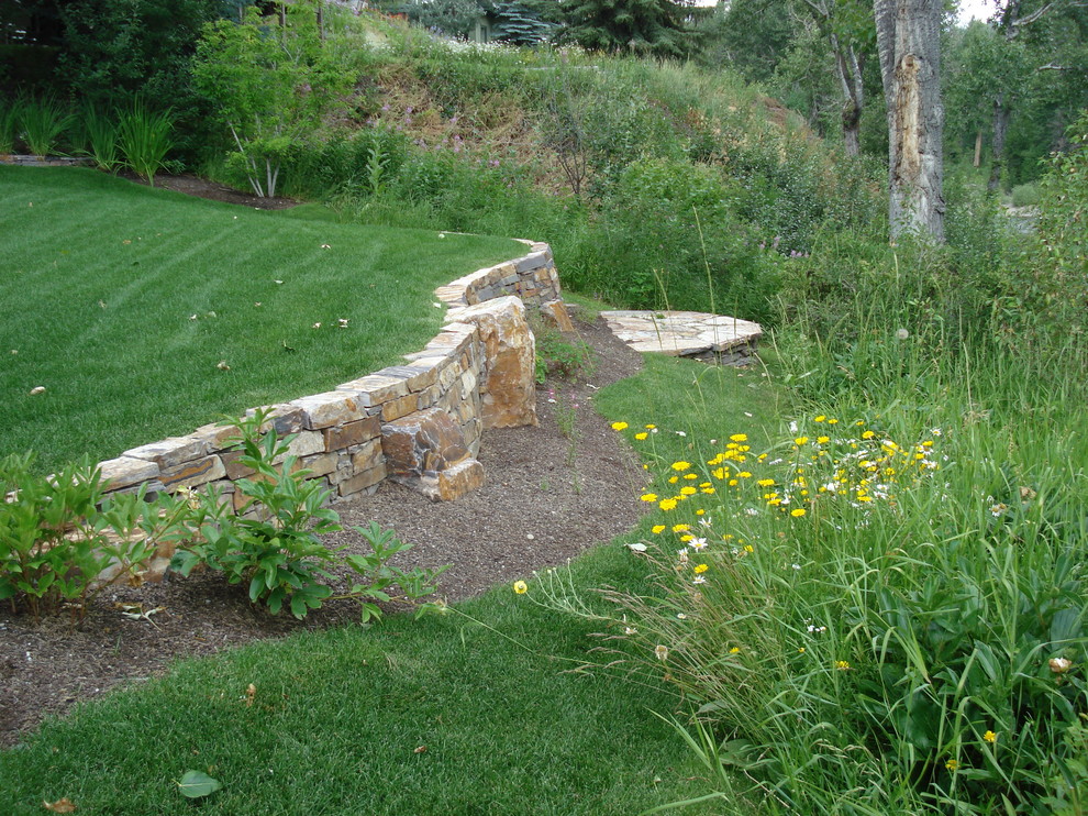 Photo of a large traditional backyard partial sun formal garden for spring in Boise with a retaining wall and natural stone pavers.