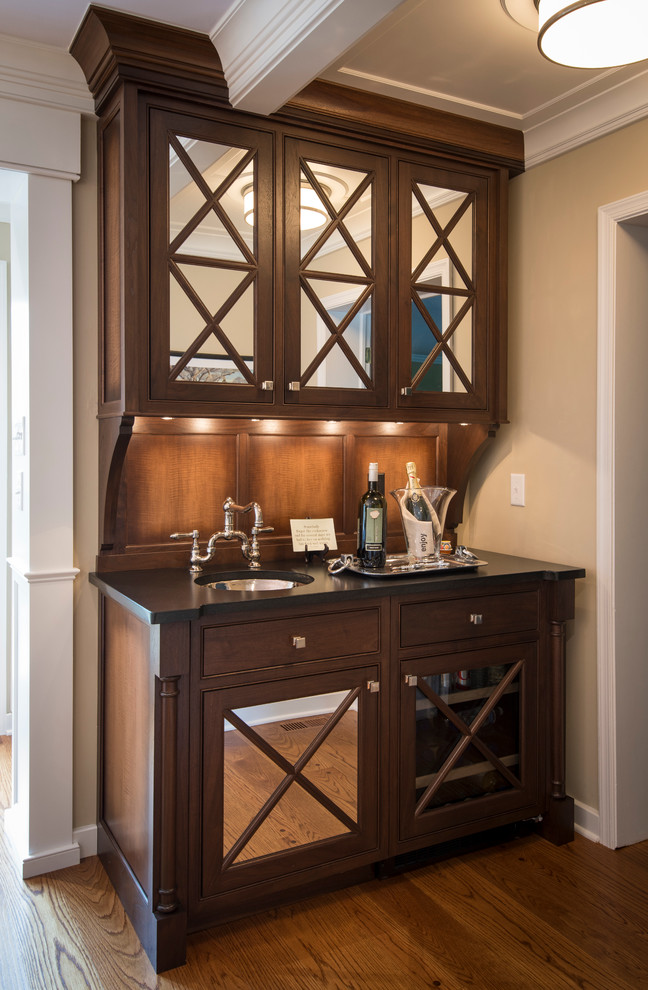 Photo of a small traditional single-wall home bar in Philadelphia with an undermount sink, glass-front cabinets, dark wood cabinets, solid surface benchtops and medium hardwood floors.