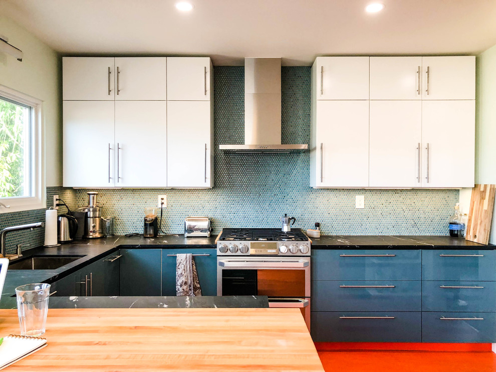 This is an example of a mid-sized contemporary u-shaped kitchen pantry in Los Angeles with flat-panel cabinets, blue splashback, stainless steel appliances, a peninsula, blue cabinets, mosaic tile splashback, black benchtop, granite benchtops, a drop-in sink, vinyl floors and orange floor.