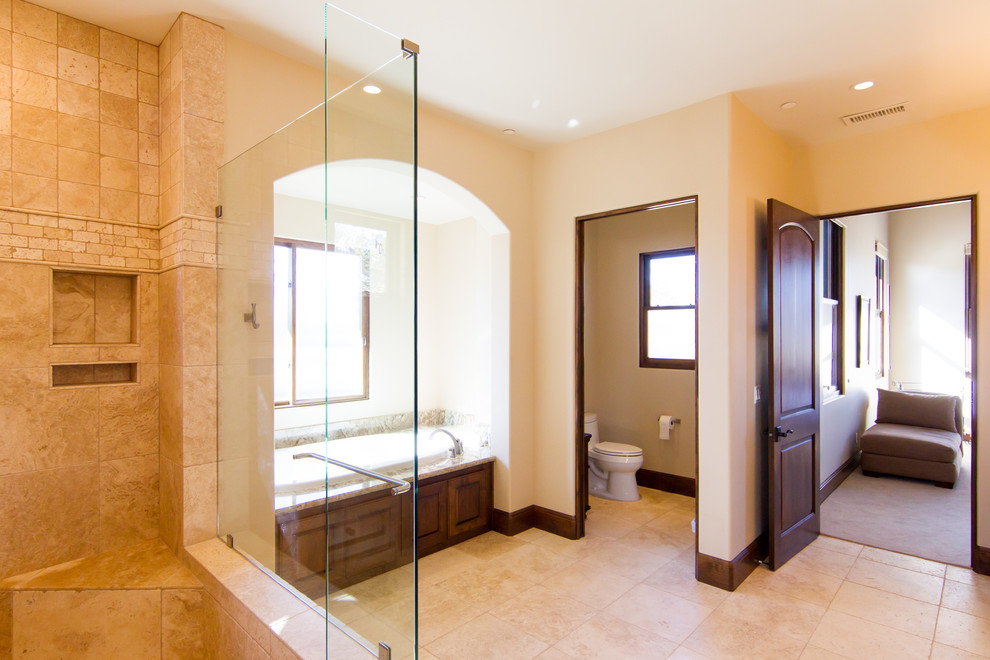 Photo of a large mediterranean master bathroom in San Luis Obispo with an undermount sink, raised-panel cabinets, beige cabinets, granite benchtops, an alcove tub, a curbless shower, a one-piece toilet, stone tile, beige walls, travertine floors and beige tile.