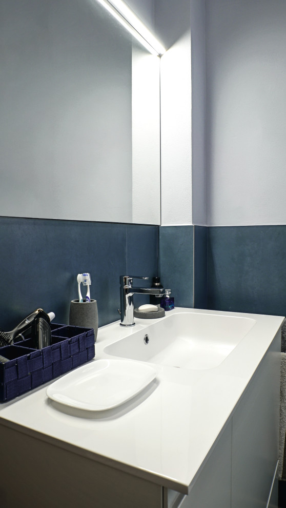 Idée de décoration pour un petit WC suspendu urbain avec des portes de placard blanches, un carrelage bleu, des carreaux de porcelaine, un mur gris, un sol en carrelage de porcelaine, un lavabo posé, un plan de toilette en surface solide, un sol marron, un plan de toilette blanc et meuble-lavabo suspendu.