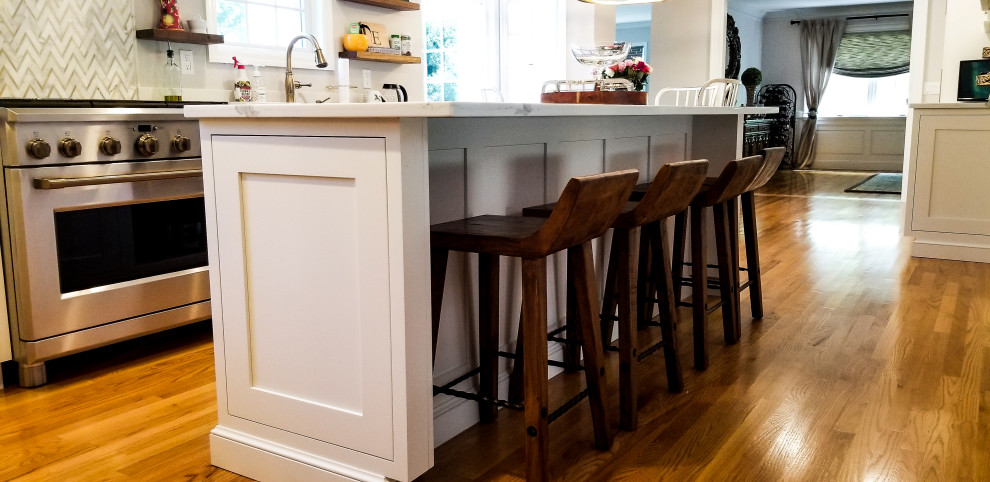 This is an example of a traditional kitchen in New York with a farmhouse sink, shaker cabinets, white cabinets, quartz benchtops, medium hardwood floors, with island and white benchtop.