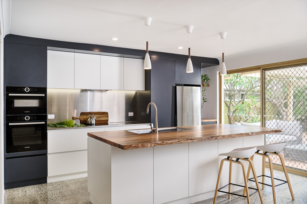 This is an example of a medium sized urban galley kitchen/diner in Perth with a built-in sink, flat-panel cabinets, black cabinets, stainless steel worktops, grey splashback, black appliances, concrete flooring, an island, grey floors and grey worktops.