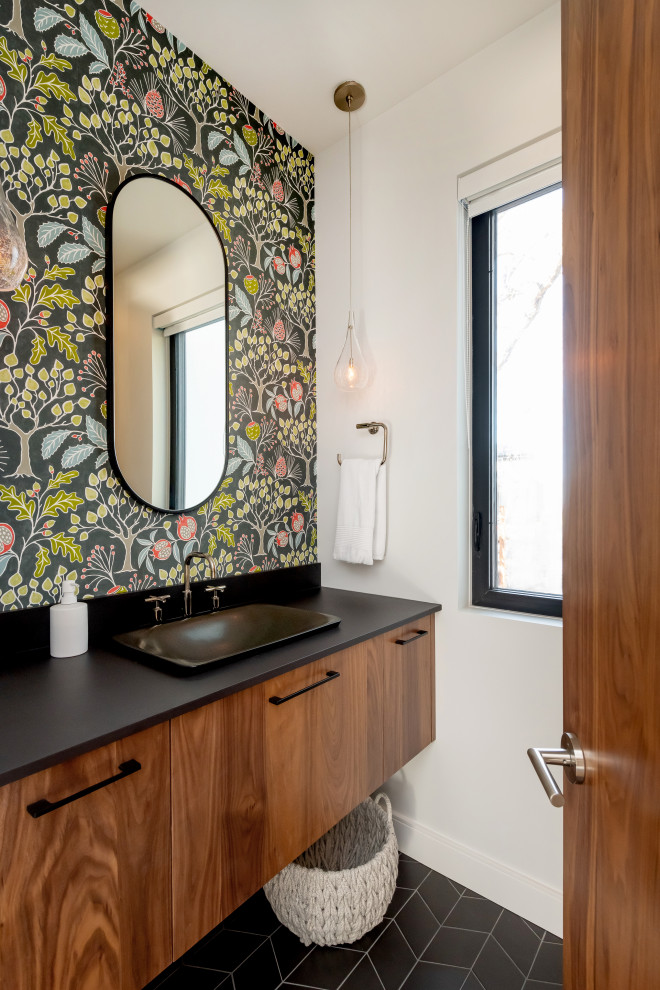 Example of a mid-sized trendy ceramic tile, black floor and wallpaper powder room design in Other with flat-panel cabinets, medium tone wood cabinets, white walls, quartz countertops, black countertops, a floating vanity and a drop-in sink