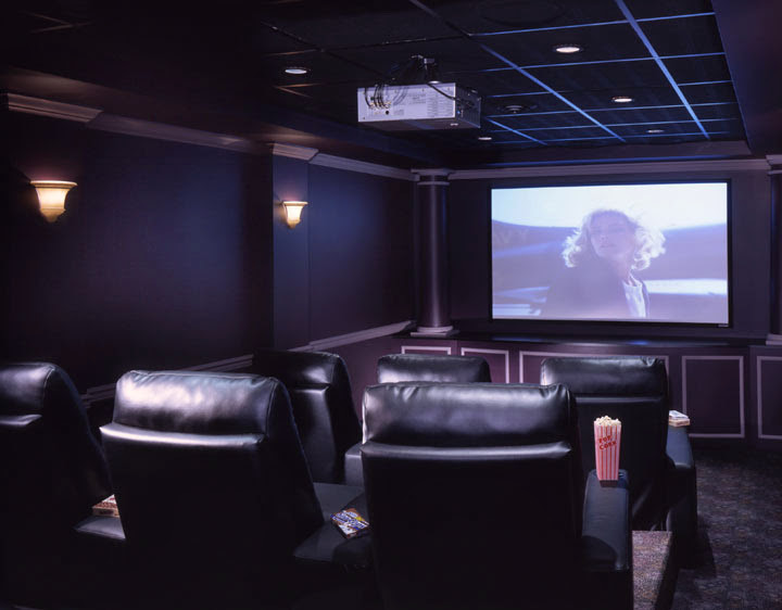 Large mountain style enclosed carpeted home theater photo with brown walls and a projector screen