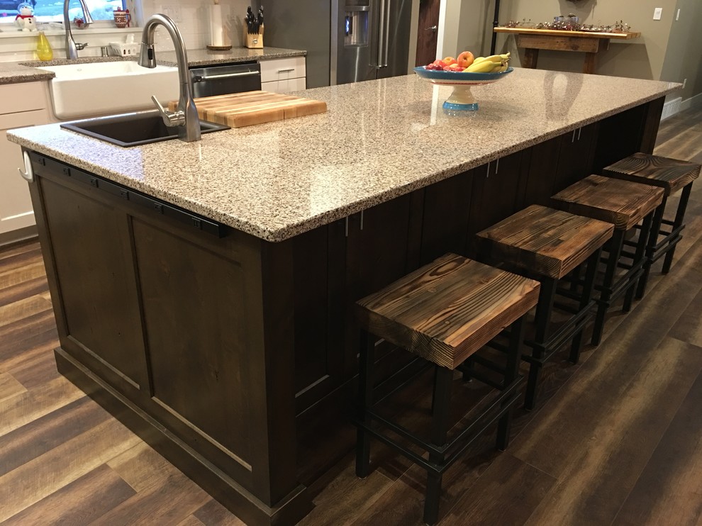 Example of a large transitional l-shaped dark wood floor and brown floor eat-in kitchen design with a farmhouse sink, shaker cabinets, white cabinets, granite countertops, white backsplash, stainless steel appliances and an island