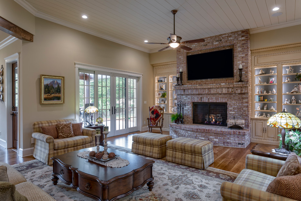 Photo of an expansive country open concept living room in Other with a library, beige walls, medium hardwood floors, a standard fireplace, a brick fireplace surround, a built-in media wall and brown floor.