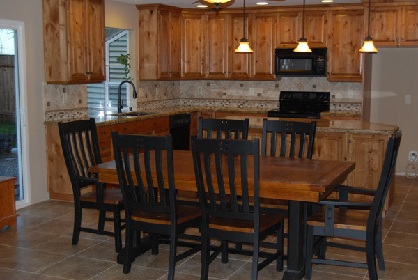 Example of a large mountain style l-shaped ceramic tile and beige floor eat-in kitchen design in Phoenix with a drop-in sink, raised-panel cabinets, medium tone wood cabinets, granite countertops, beige backsplash, stone tile backsplash, black appliances and an island