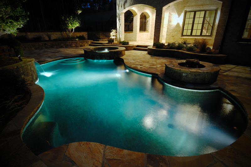 Design ideas for a large contemporary backyard custom-shaped pool in Miami with a water feature and natural stone pavers.