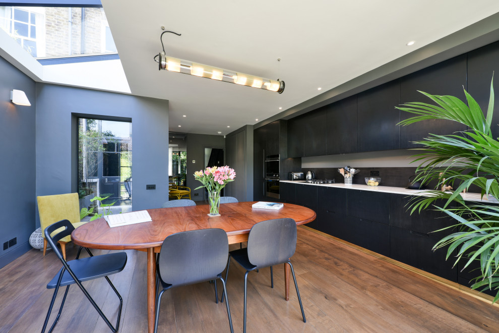 Design ideas for a contemporary single-wall eat-in kitchen in London with flat-panel cabinets, black cabinets, stainless steel appliances, dark hardwood floors, brown floor and white benchtop.