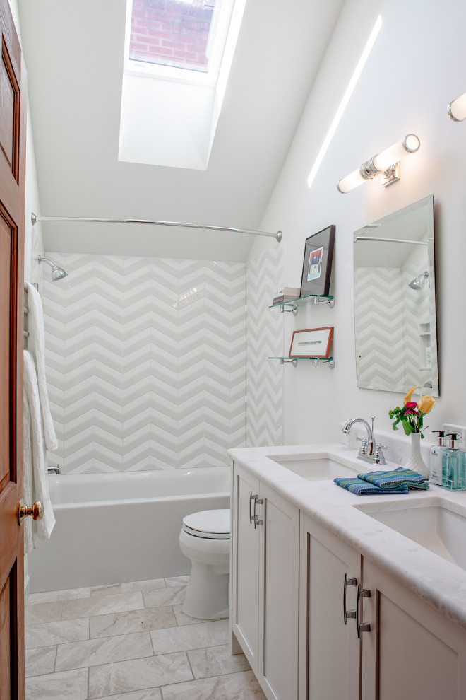 Photo of a mid-sized transitional kids bathroom in Detroit with shaker cabinets, white cabinets, an alcove tub, a two-piece toilet, ceramic tile, white walls, travertine floors, an undermount sink, marble benchtops, beige floor, a shower curtain, a built-in vanity, vaulted, a shower/bathtub combo, gray tile, white tile, white benchtops and a double vanity.
