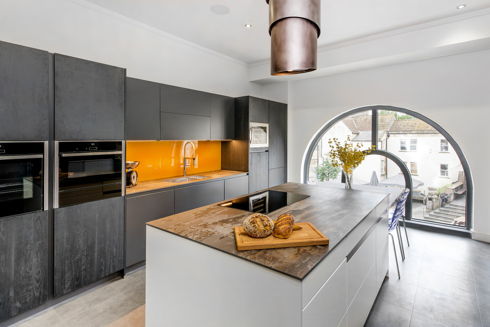 Photo of a large contemporary u-shaped eat-in kitchen in Other with a drop-in sink, black cabinets, glass sheet splashback, multiple islands, grey floor, yellow splashback and black appliances.
