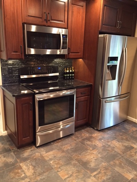 Transitional u-shaped porcelain tile enclosed kitchen photo with an undermount sink, medium tone wood cabinets, granite countertops, black backsplash, mosaic tile backsplash, stainless steel appliances and no island