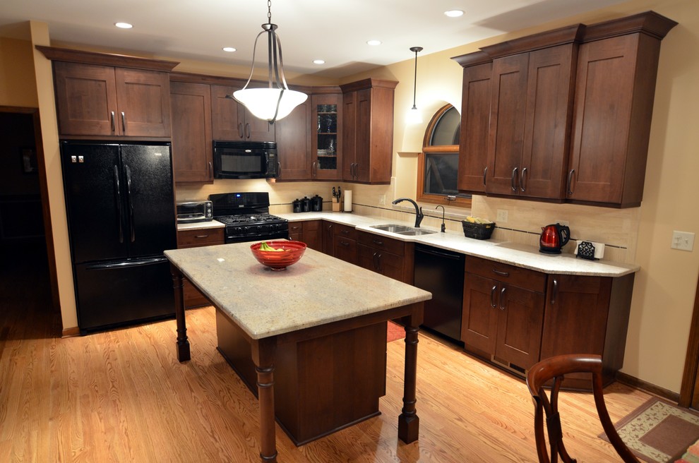 This is an example of a traditional l-shaped eat-in kitchen in Chicago with an undermount sink, shaker cabinets, medium wood cabinets, granite benchtops, brown splashback, stone tile splashback and black appliances.