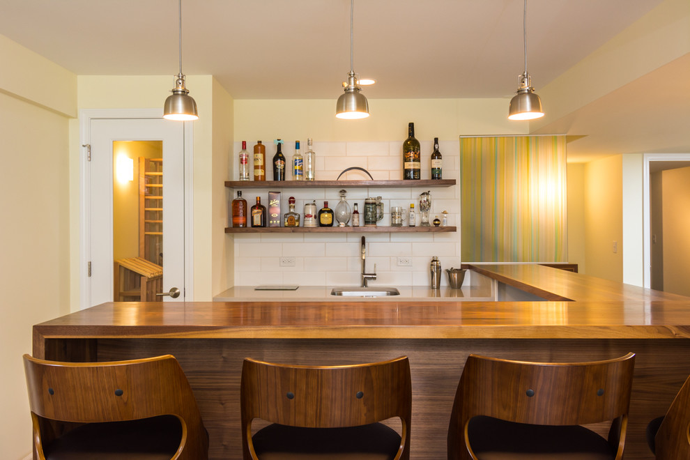 This is an example of an expansive midcentury u-shaped seated home bar in Detroit with wood benchtops, white splashback, subway tile splashback, brown floor and vinyl floors.