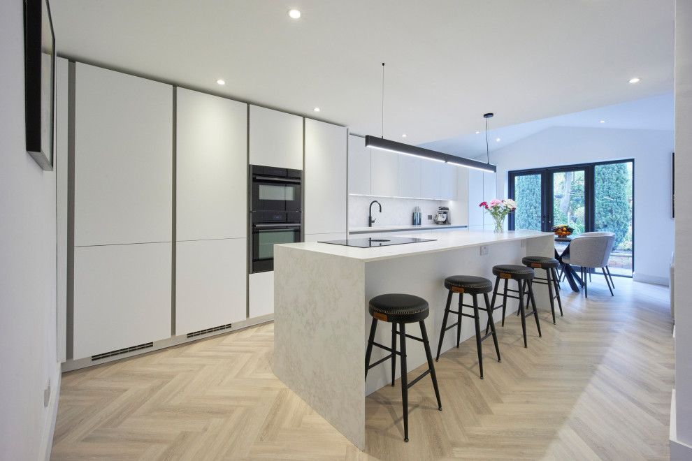 Inspiration for a large modern single-wall open plan kitchen in Other with flat-panel cabinets, white cabinets, quartzite benchtops, white splashback, black appliances, with island, beige floor and white benchtop.