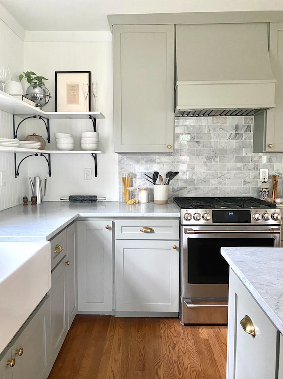 Photo of a mid-sized kitchen in Austin with a farmhouse sink, shaker cabinets, green cabinets, marble benchtops, white splashback, stainless steel appliances, medium hardwood floors, with island, brown floor and grey benchtop.