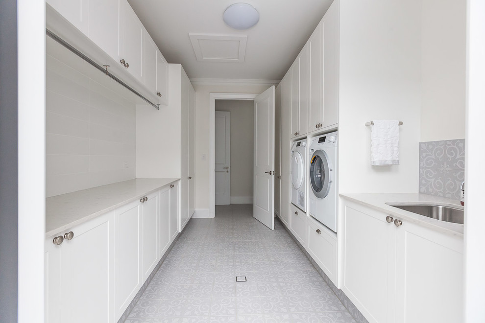 This is an example of a large traditional galley dedicated laundry room in Gold Coast - Tweed with a drop-in sink, shaker cabinets, white cabinets, quartz benchtops, white walls, porcelain floors, a side-by-side washer and dryer and white floor.