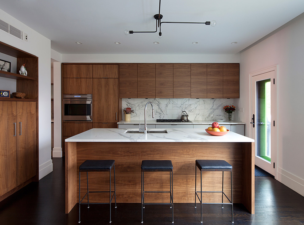 Photo of a mid-sized contemporary galley eat-in kitchen in New York with medium wood cabinets, dark hardwood floors, with island, an undermount sink, flat-panel cabinets, marble benchtops, white splashback, stone tile splashback, stainless steel appliances and brown floor.