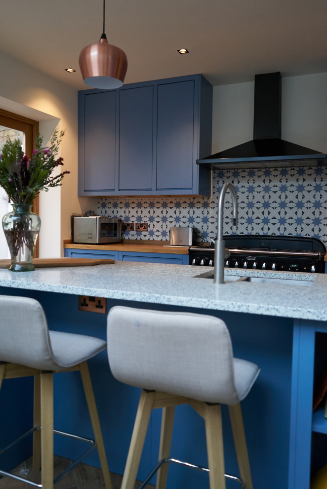 Large contemporary galley open plan kitchen in London with an integrated sink, flat-panel cabinets, blue cabinets, recycled glass benchtops, blue splashback, porcelain splashback, white appliances, light hardwood floors, with island, blue benchtop and vaulted.