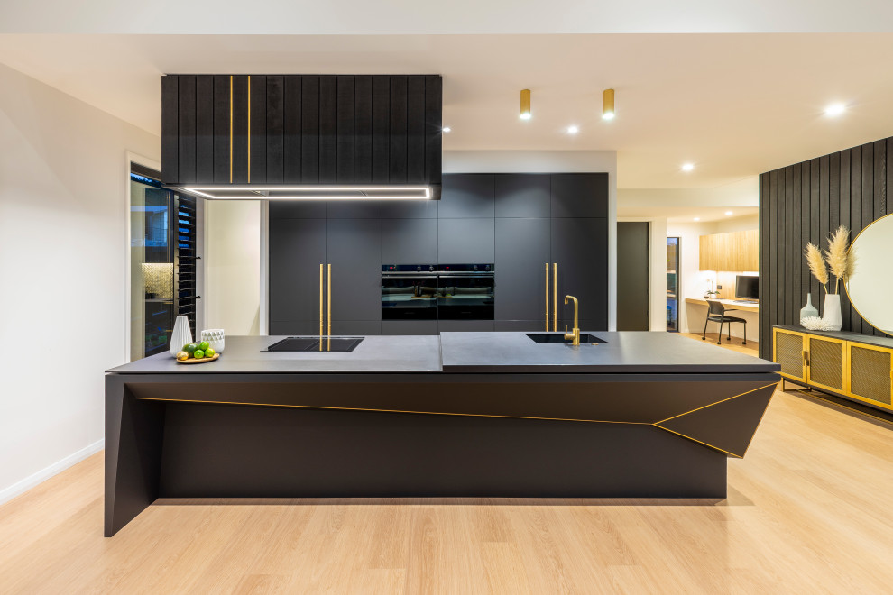 This is an example of a large contemporary galley open plan kitchen in Auckland with an undermount sink, black cabinets, ceramic splashback, black appliances, with island and black benchtop.