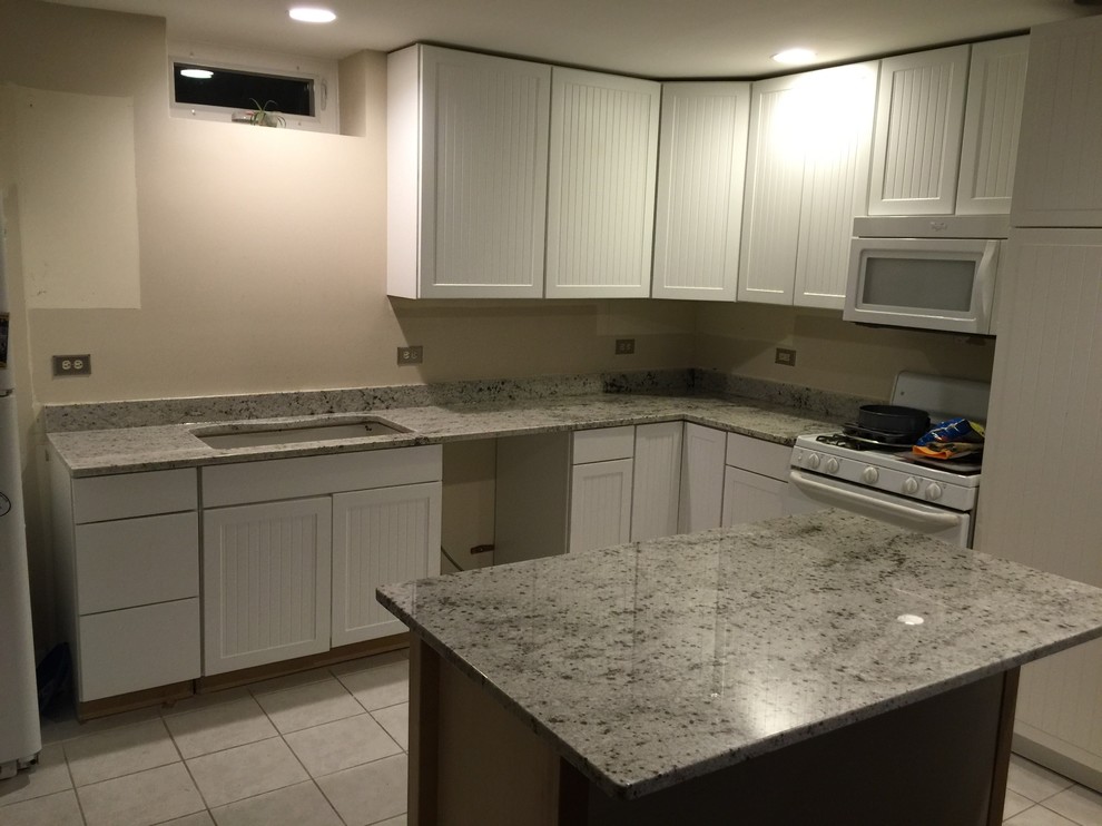 Mid-sized transitional l-shaped ceramic tile enclosed kitchen photo in Chicago with an undermount sink, flat-panel cabinets, white cabinets, granite countertops, white appliances and an island