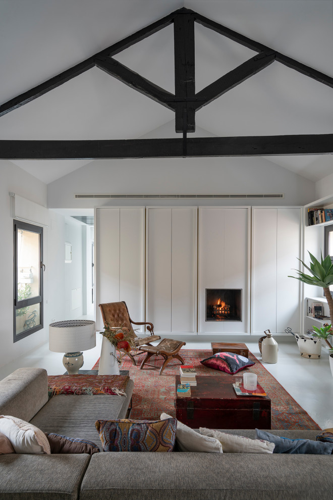 Design ideas for a mid-sized contemporary loft-style living room in Madrid with white walls, concrete floors, a standard fireplace, grey floor, exposed beam, vaulted and a library.