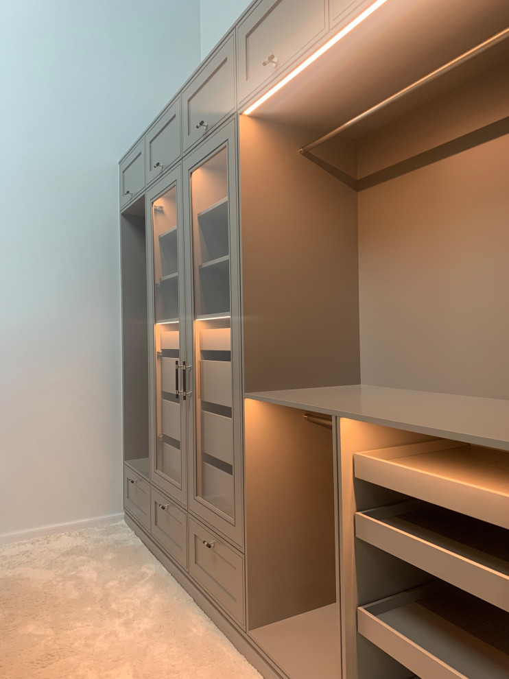 This is an example of a mid-sized scandinavian gender-neutral walk-in wardrobe in Copenhagen with glass-front cabinets, grey cabinets, carpet and white floor.