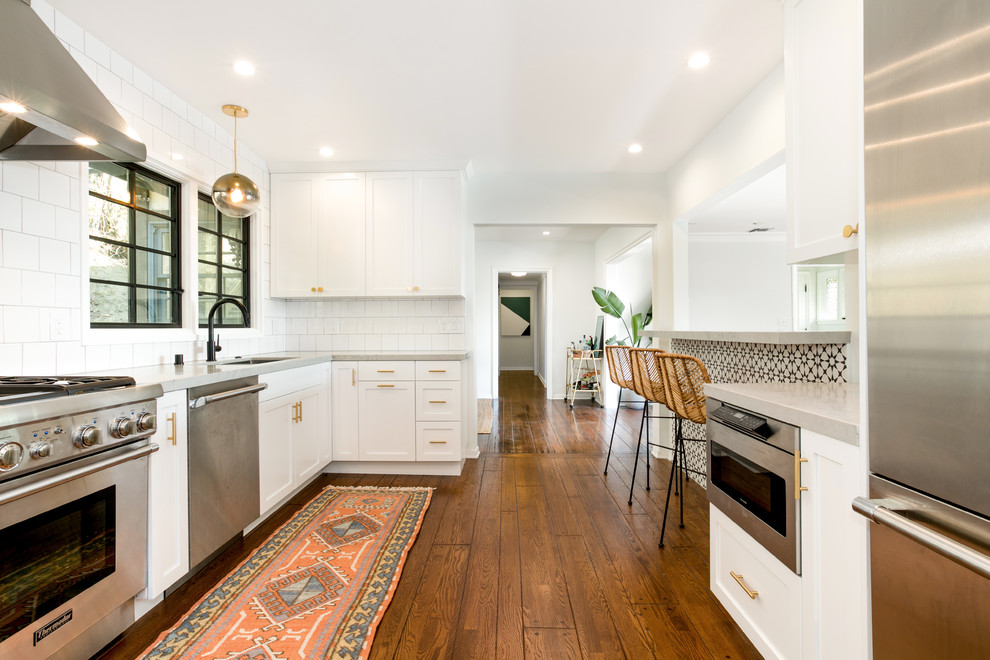 Photo of a large transitional u-shaped eat-in kitchen in Los Angeles with a drop-in sink, shaker cabinets, white cabinets, quartz benchtops, white splashback, ceramic splashback, stainless steel appliances, medium hardwood floors, brown floor and grey benchtop.