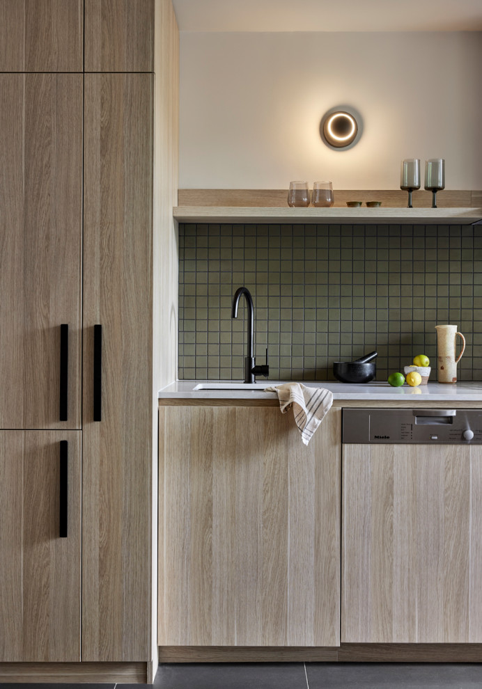Design ideas for a small scandinavian single-wall open plan kitchen in Melbourne with an undermount sink, flat-panel cabinets, light wood cabinets, quartz benchtops, green splashback, ceramic splashback, black appliances, light hardwood floors, no island, yellow floor and grey benchtop.