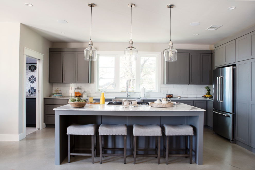 Large transitional l-shaped eat-in kitchen in Austin with a farmhouse sink, shaker cabinets, grey cabinets, marble benchtops, white splashback, glass tile splashback, stainless steel appliances, concrete floors, with island and grey floor.